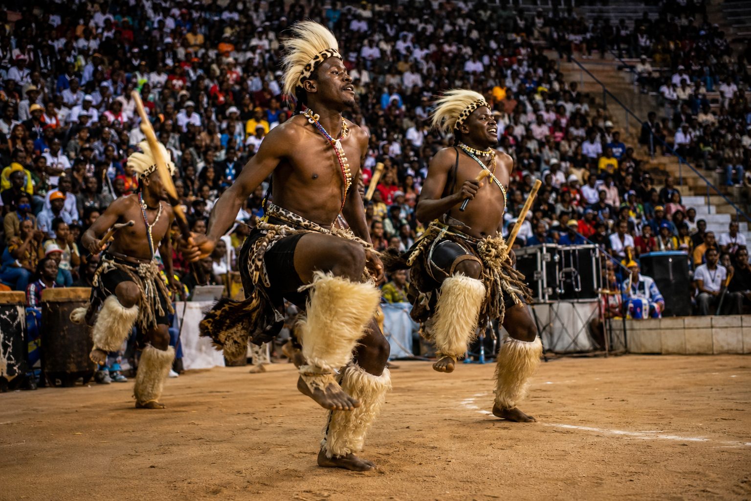 Dancers in traditional dress performing to a large seated arena crowd during a music competition final